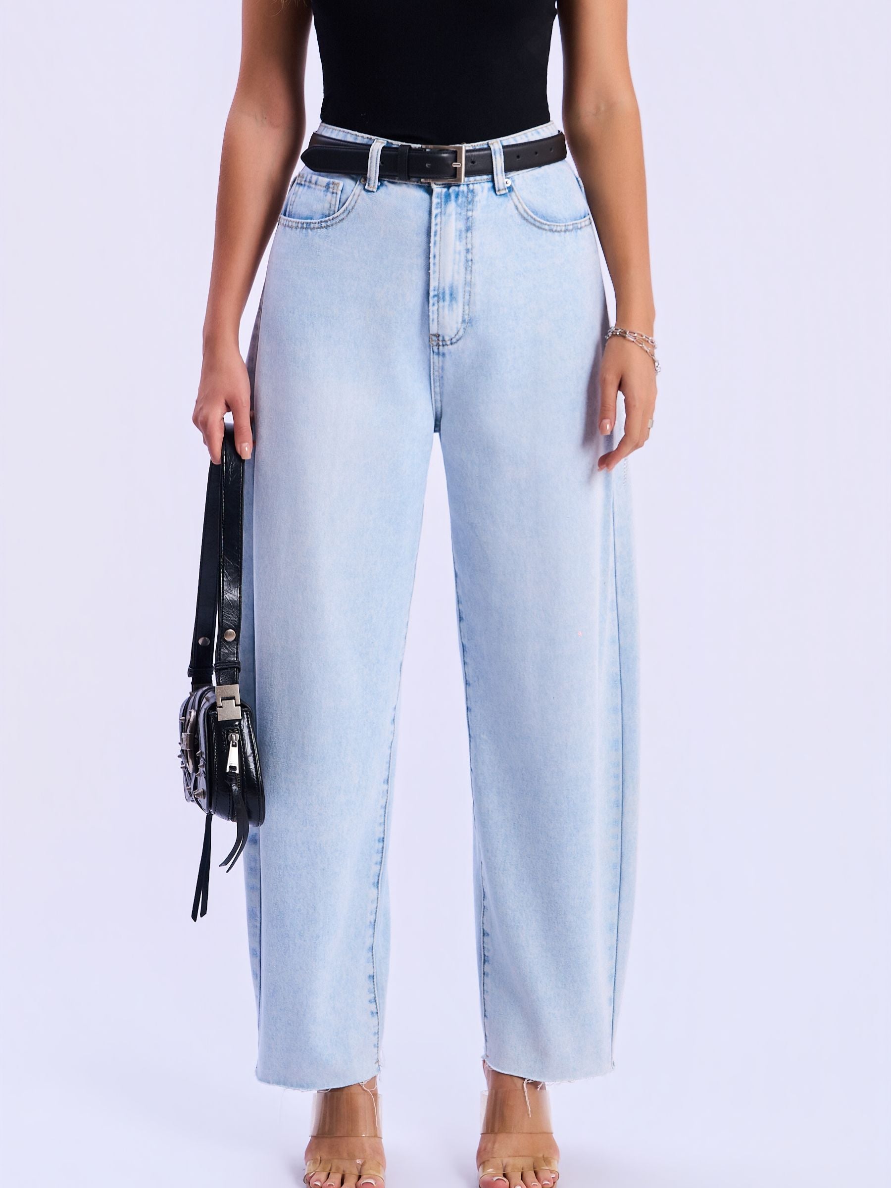 Person wearing light blue jeans with a black belt and holding a black handbag on a white background
