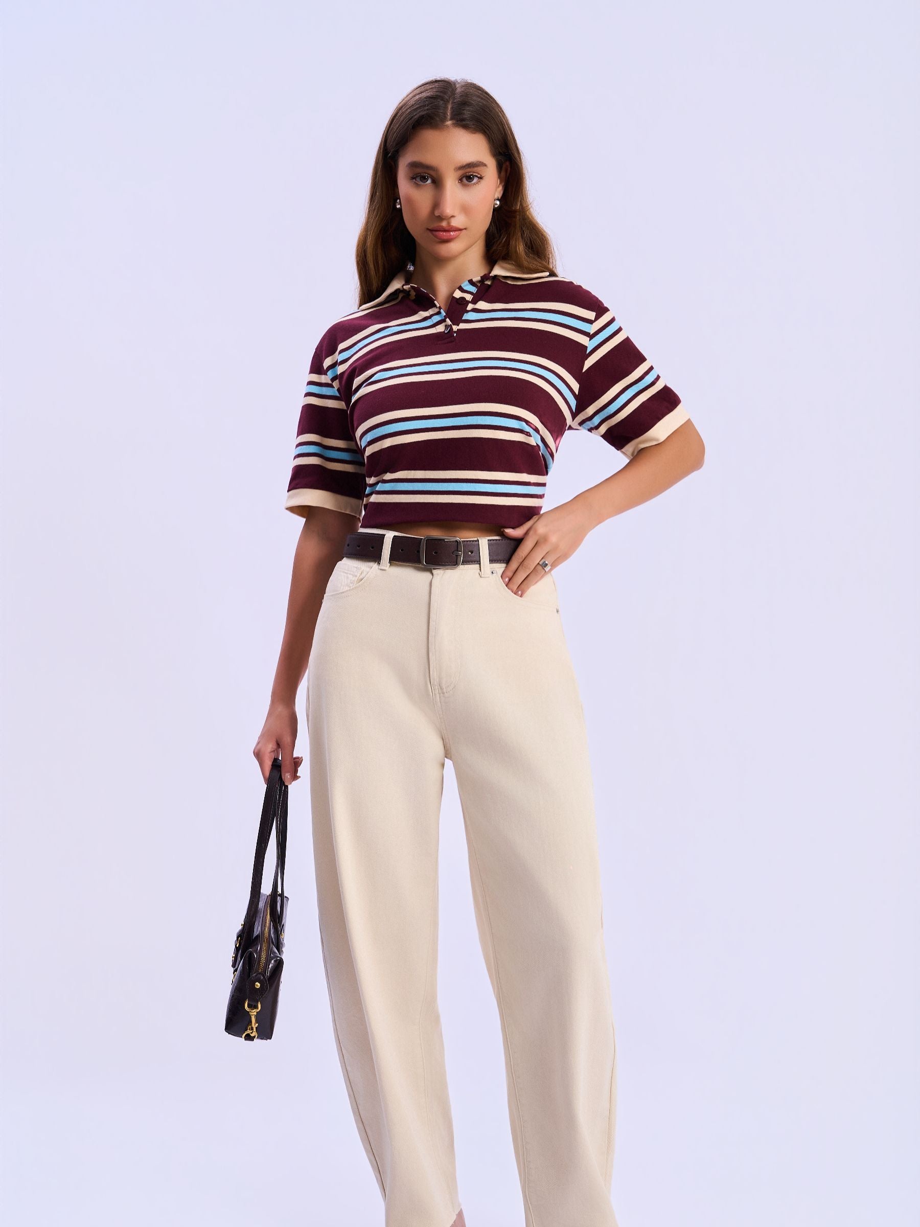 Woman wearing a striped shirt and beige pants against a light purple background